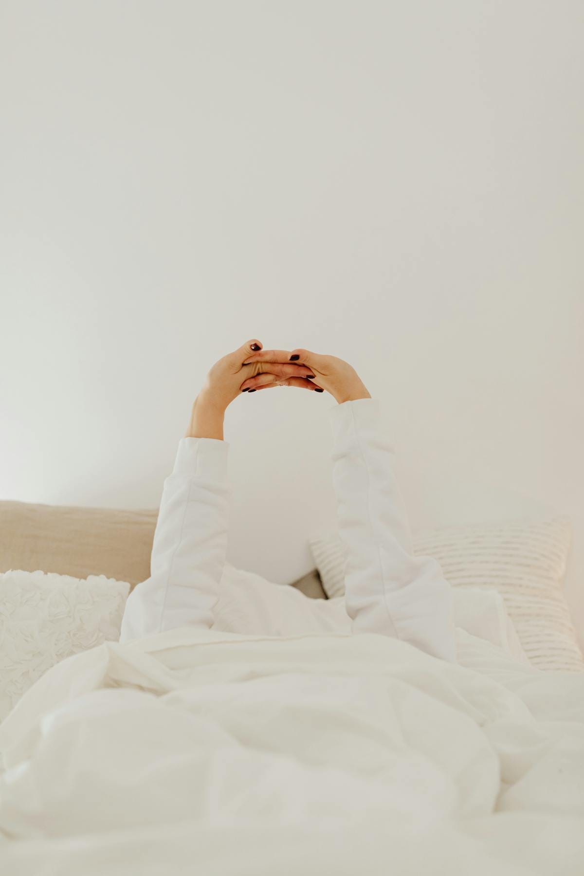 Person stretching and relaxing in bed with white sheets in the morning, representing quality rest and recovery for fitness progress