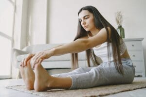 Person stretching gently on a rug in a light-filled room, focusing on mobility and recovery after a home workout